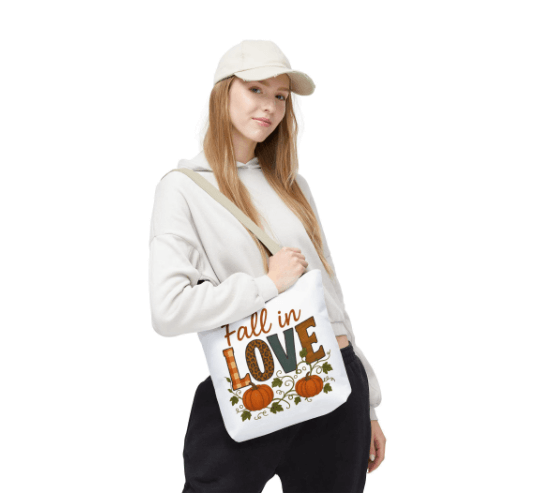 Person holding a tote bag with 'Fall in Love' text and pumpkins on a white background