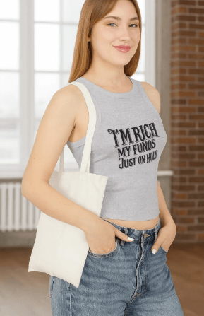Woman wearing a gray tank top with text, holding a white tote bag indoors.