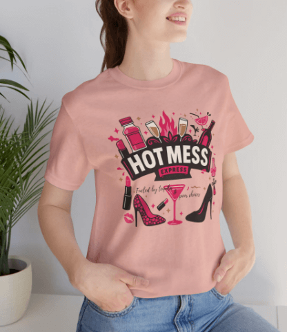 Person wearing a pink t-shirt with a graphic design and text, standing against a light background.