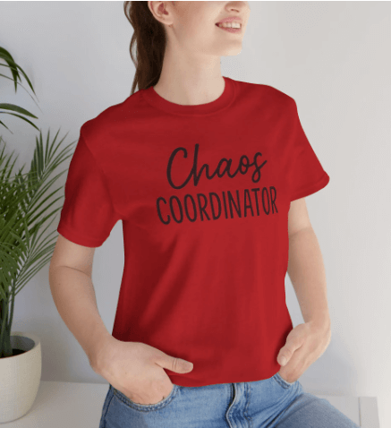 Person wearing a red t-shirt with 'Chaos Coordinator' text, standing against a white wall.
