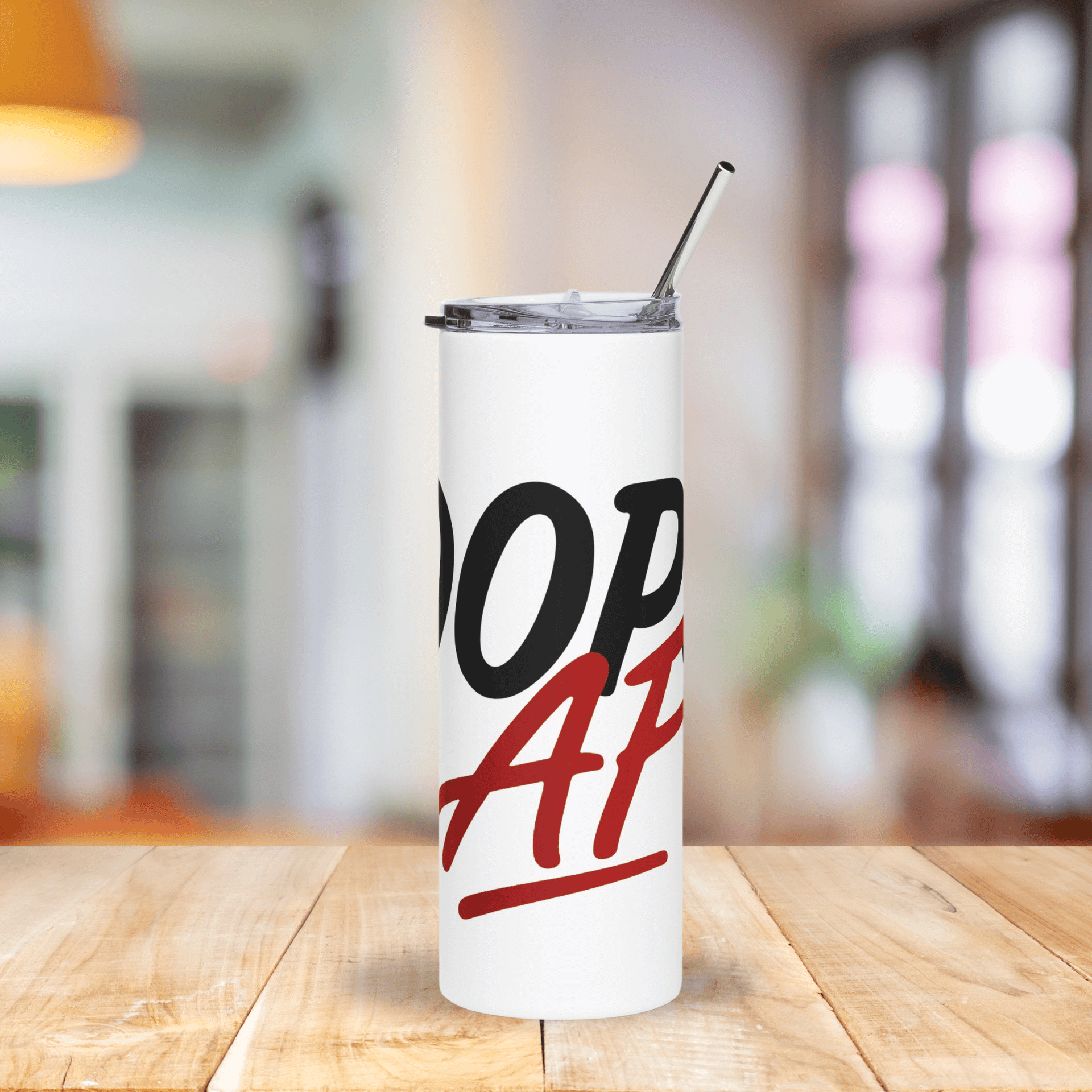 White tumbler with black and red text on a wooden table with a blurred background