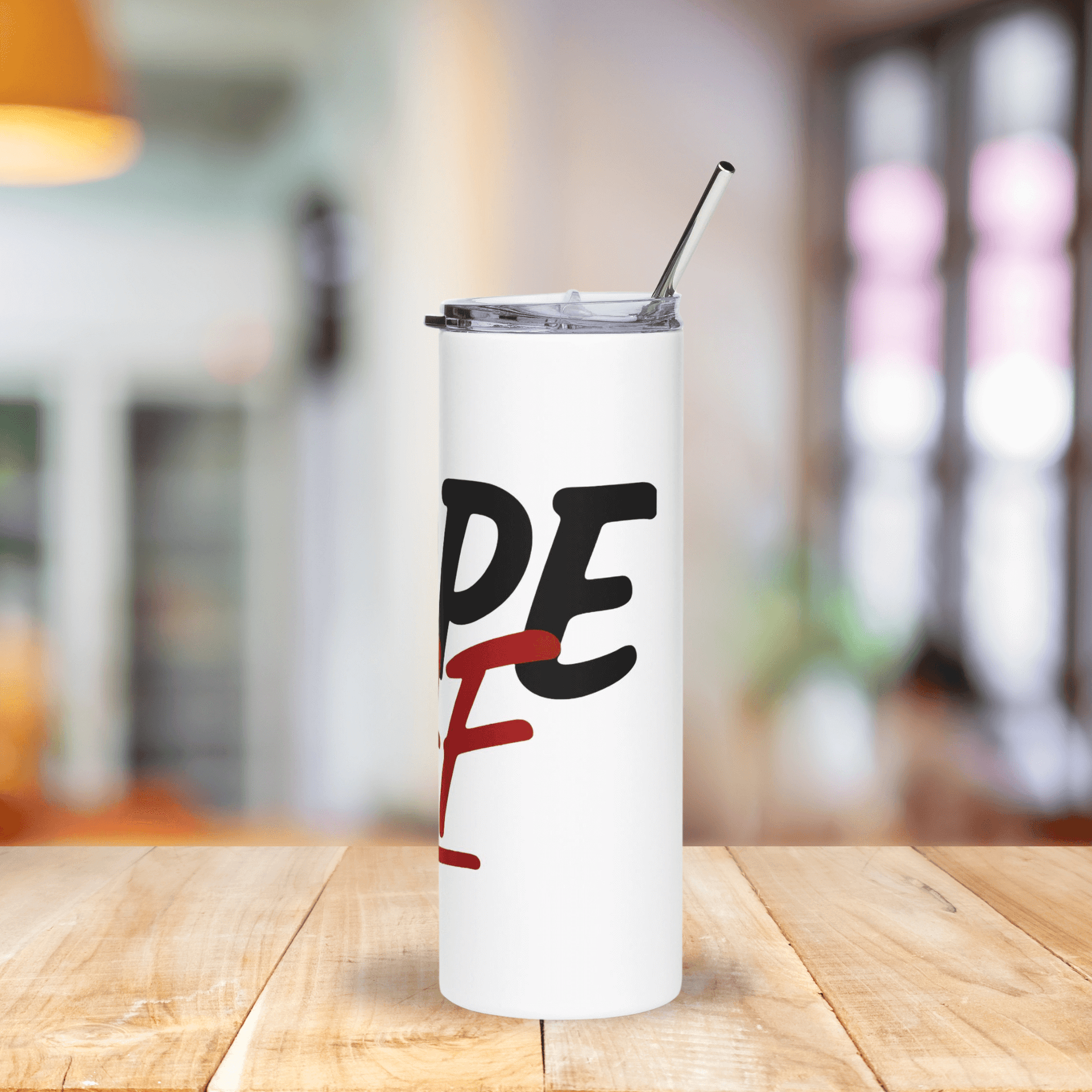 White tumbler with black and red text on a wooden table with a blurred background
