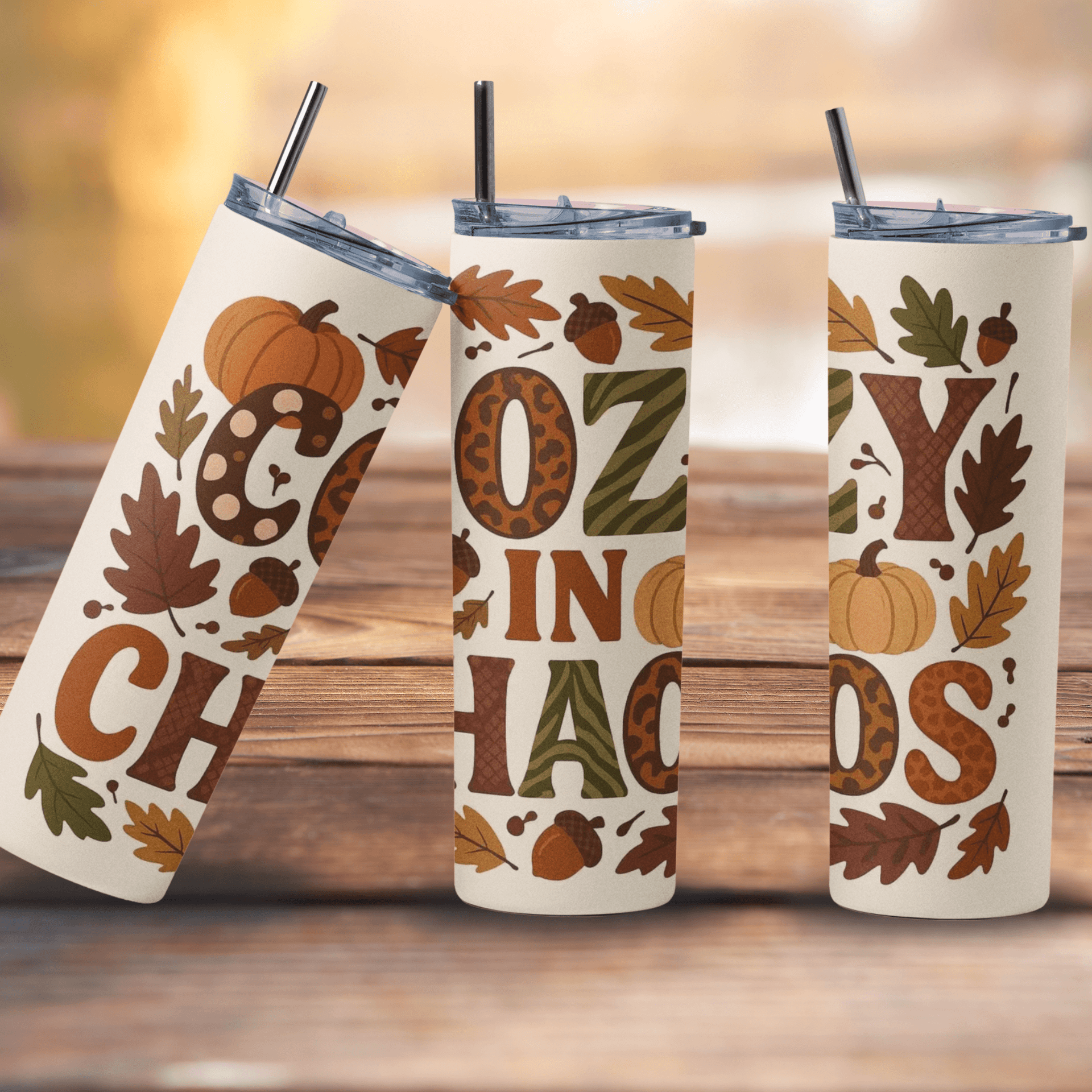 Three white tumblers with autumn-themed designs on a wooden surface.