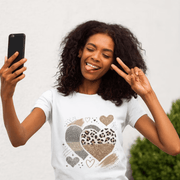 Woman wearing a white t-shirt with heart designs, taking a selfie against a plain background.