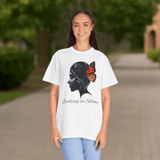 Woman wearing a white t-shirt with a graphic design of a woman's face with a butterfly on her shoulder, standing outdoors.