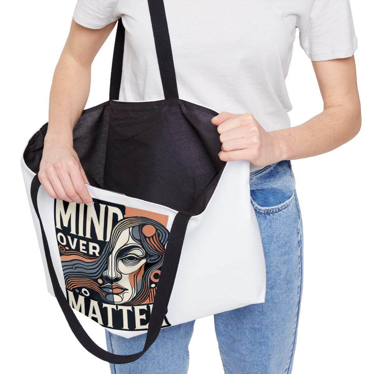 Person holding a tote bag with a design and text, wearing a white shirt and blue jeans.