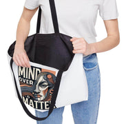 Person holding a tote bag with a design and text, wearing a white shirt and blue jeans.