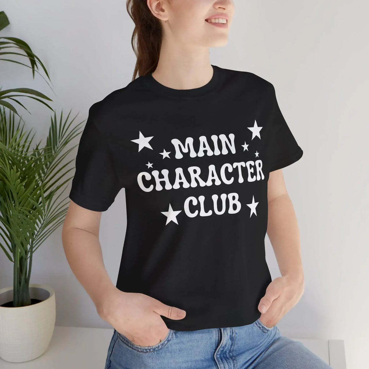 Person wearing a black t-shirt with 'MAIN CHARACTER CLUB' text and stars, standing against a light background.