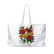 White tote bag with red roses, a dagger, and 'Delicate But Deadly' text on a white background