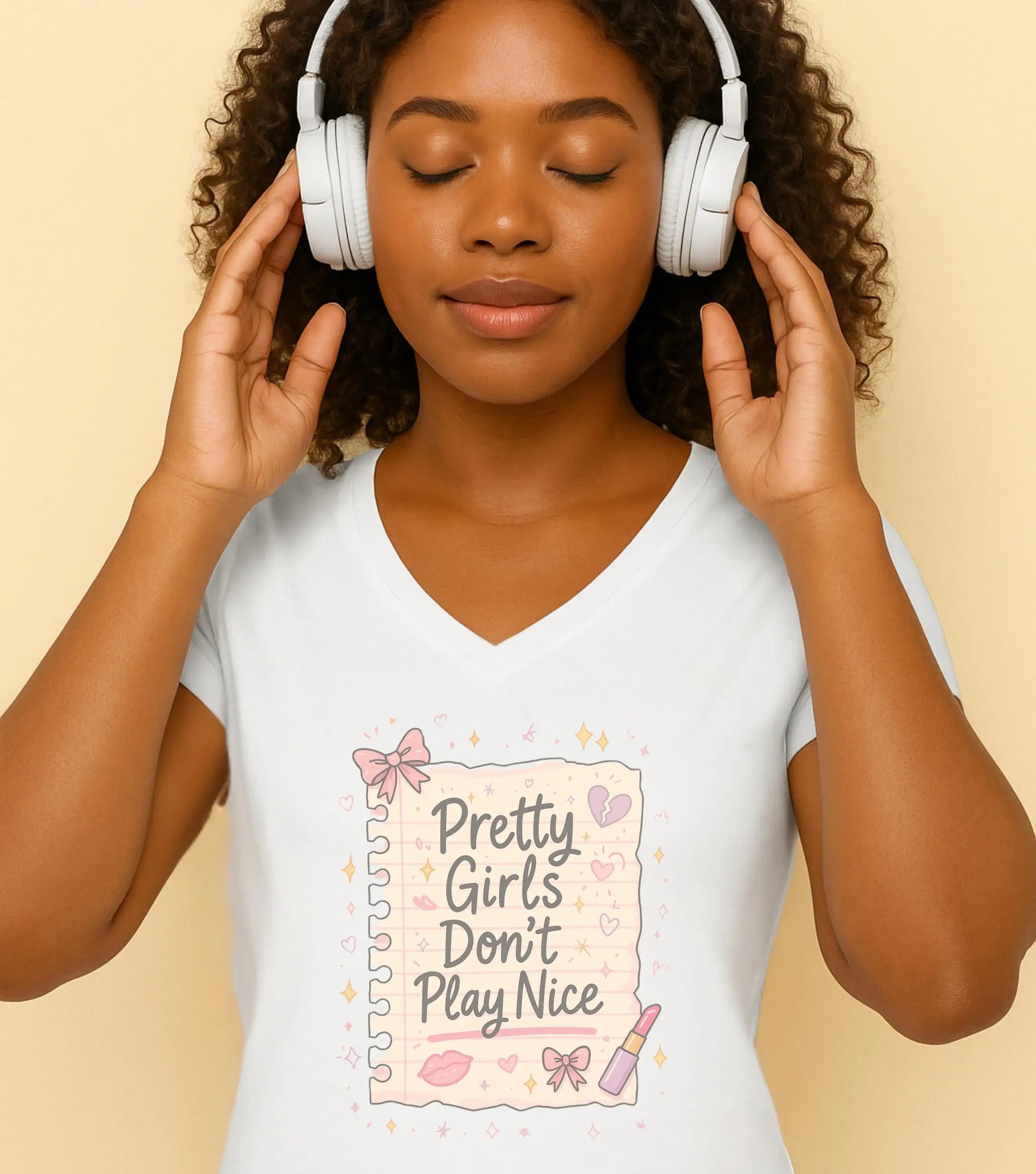 Woman wearing headphones with a t-shirt featuring 'Pretty Girls Don't Play Nice' text on a beige background