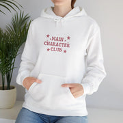 White hoodie with 'Main Character Club' text and stars worn by a person, against a neutral background.
