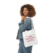 Woman holding a tote bag with 'Main Character Club' text on a white background