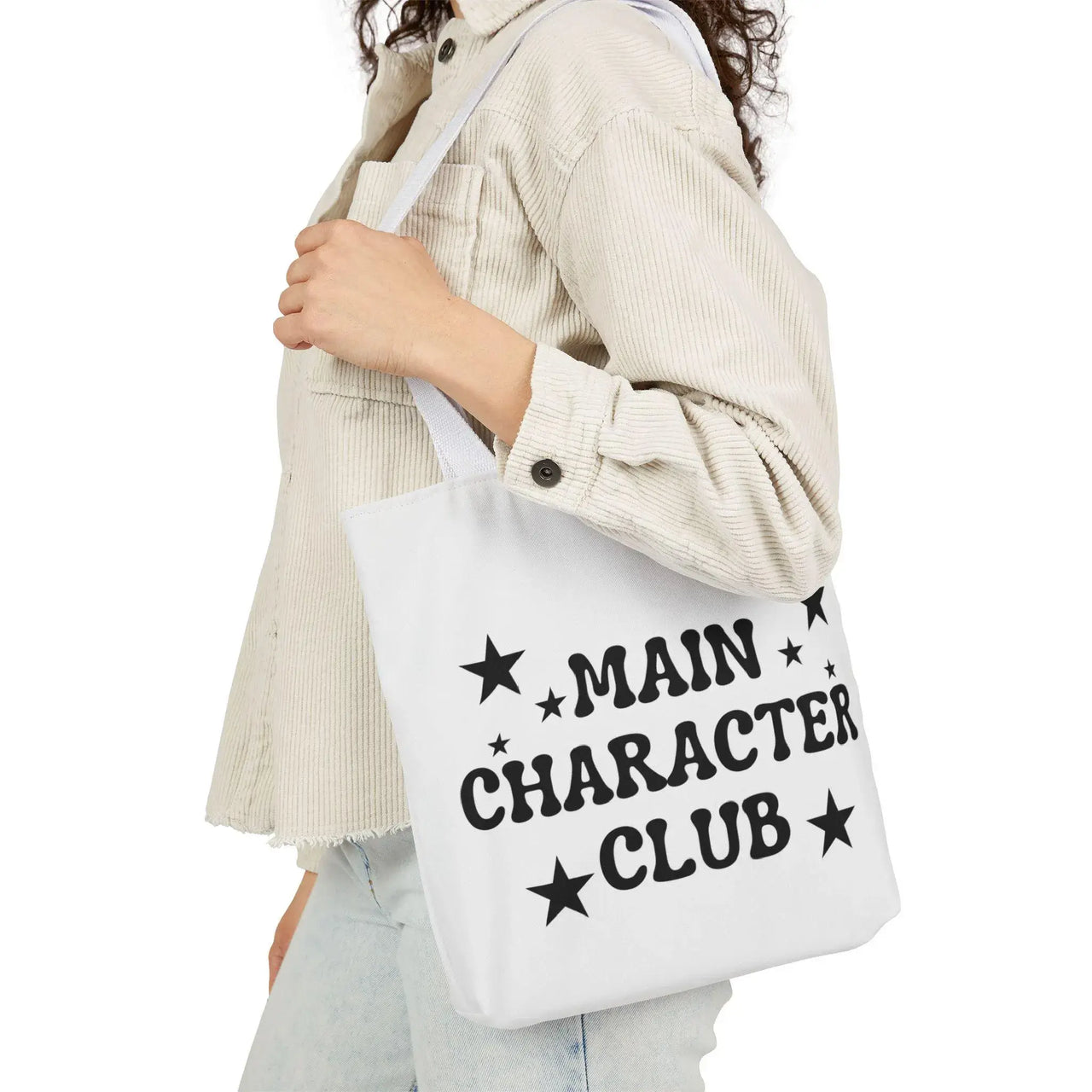 Person holding a tote bag with 'Main Character Club' text and stars.