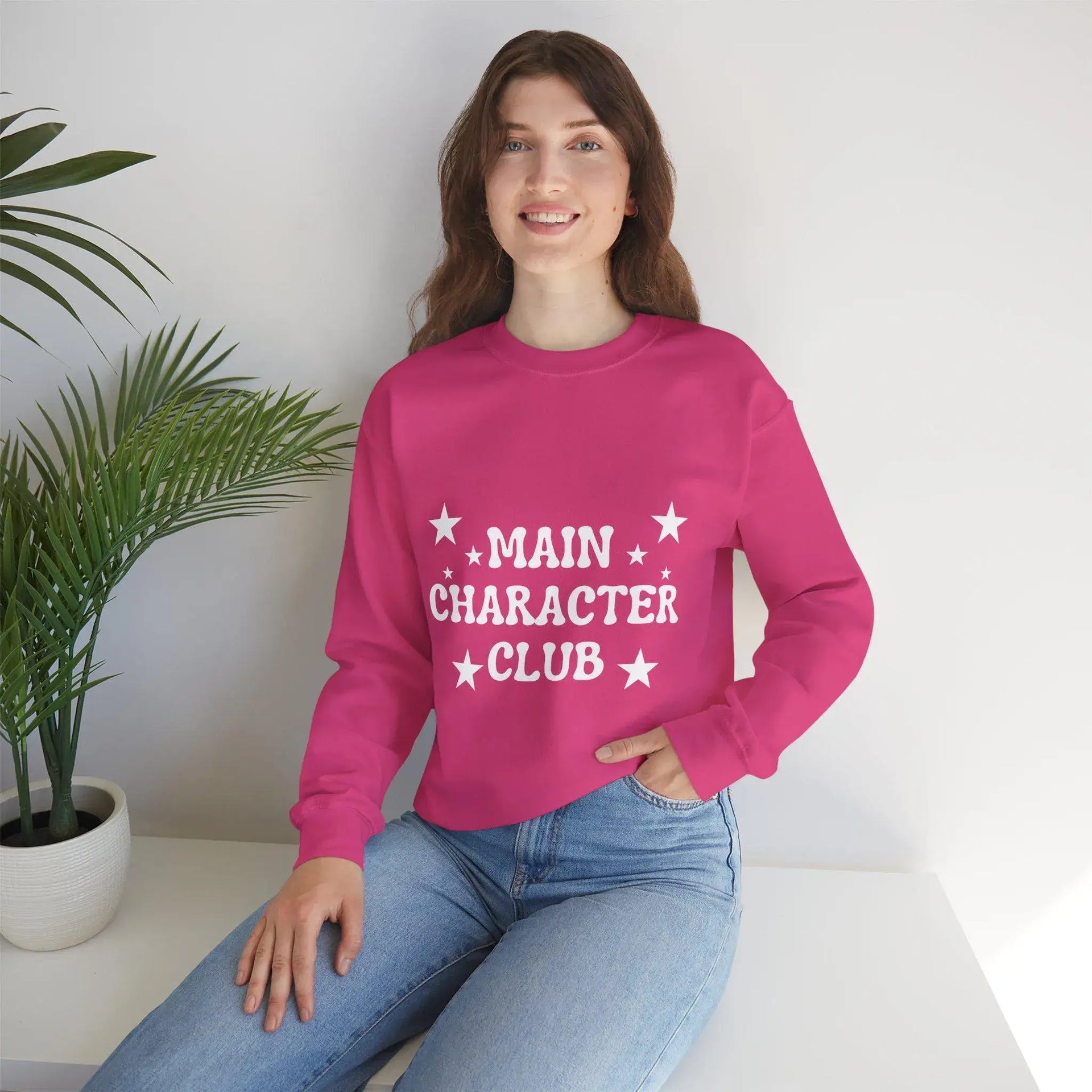 Person wearing a pink sweatshirt with 'MAIN CHARACTÓR CLUB' text, sitting indoors.