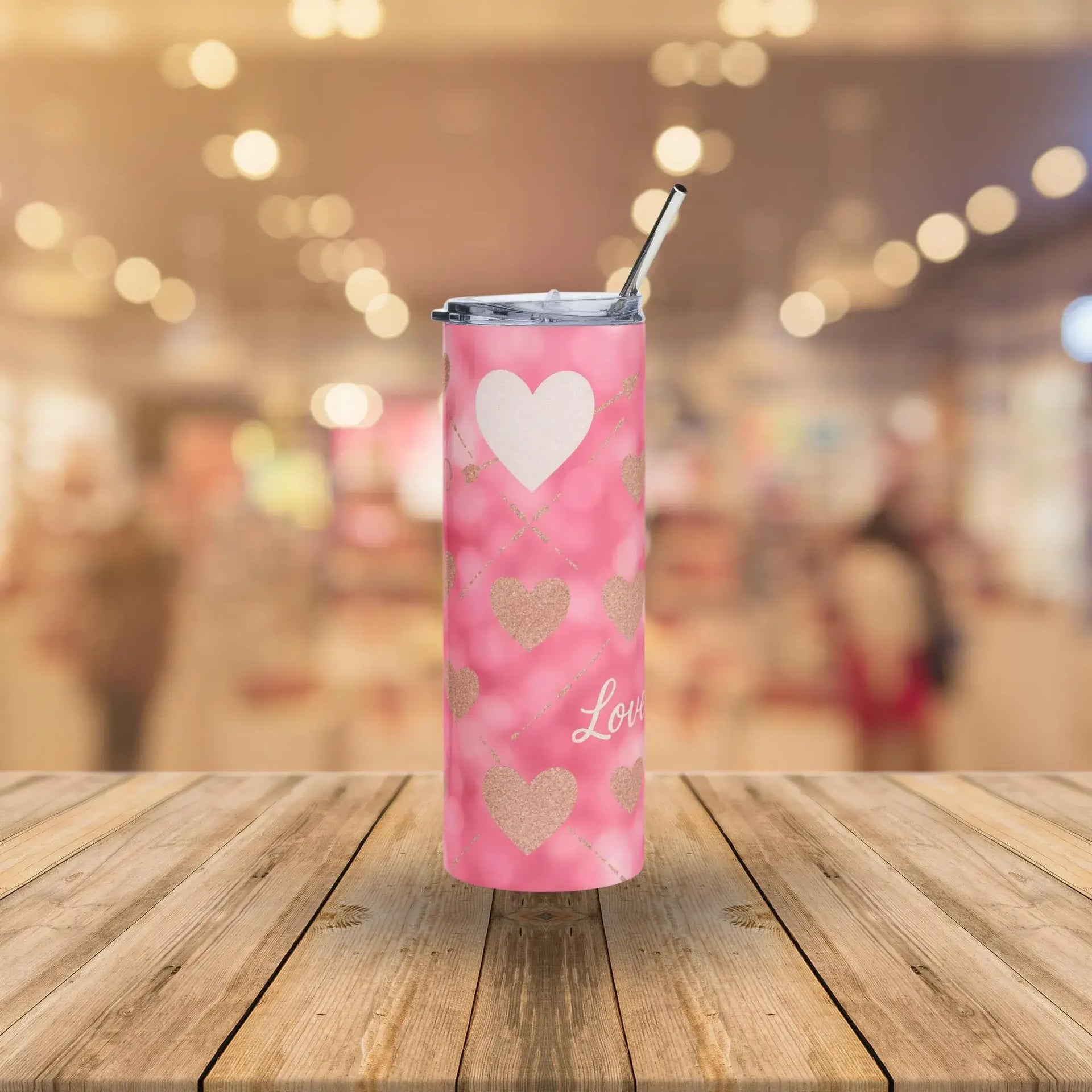 Pink tumbler with heart designs and 'Love' text on a wooden surface with a blurred background