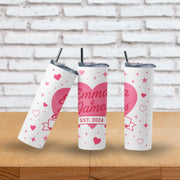 Three personalized tumblers with hearts and text on a wooden surface and brick wall background.