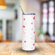 White tumbler with pink heart and star patterns on a wooden table with a blurred background