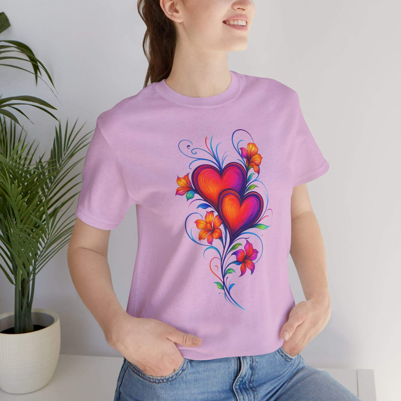 Person wearing a purple t-shirt with a colorful heart design, standing next to a plant.