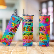 Three colorful tumblers with autism awareness designs on a wooden surface.