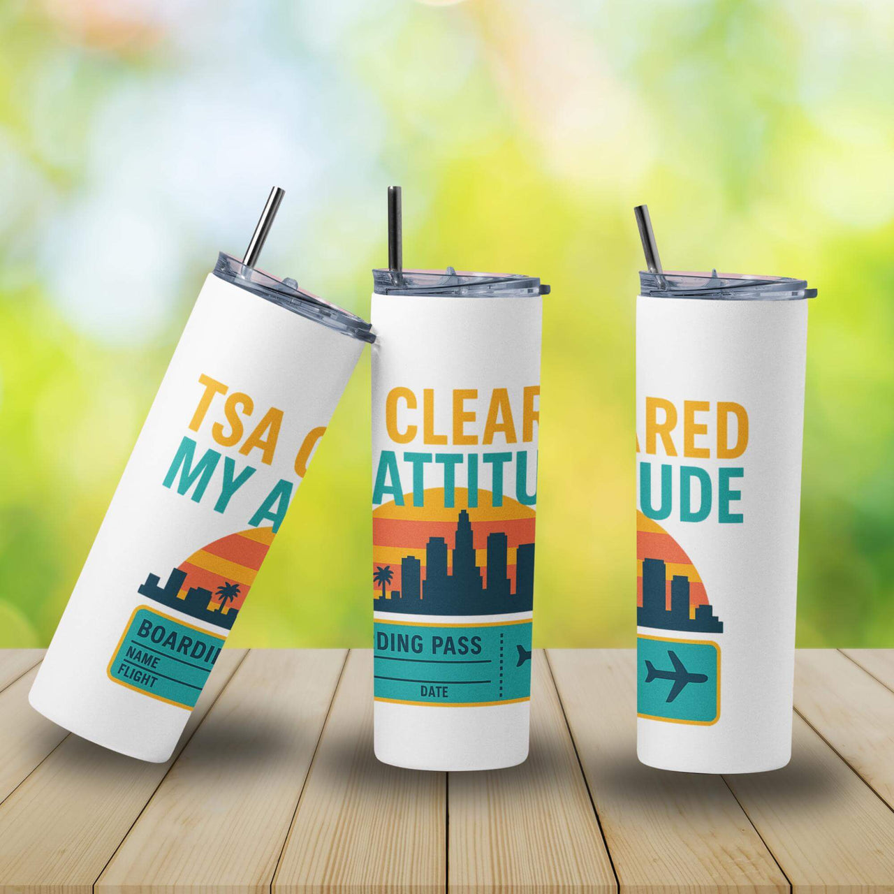 Three white tumblers with colorful designs and text on a wooden surface with a blurred green background.