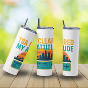 Three white tumblers with colorful designs and text on a wooden surface with a blurred green background.