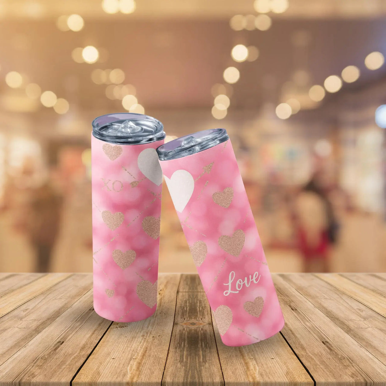 Pink tumblers with heart designs and 'Love' text on a wooden surface with a blurred background