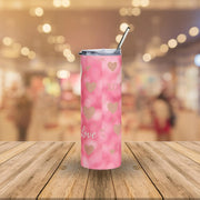 Pink tumbler with heart patterns and 'love' text on a wooden surface with a blurred background