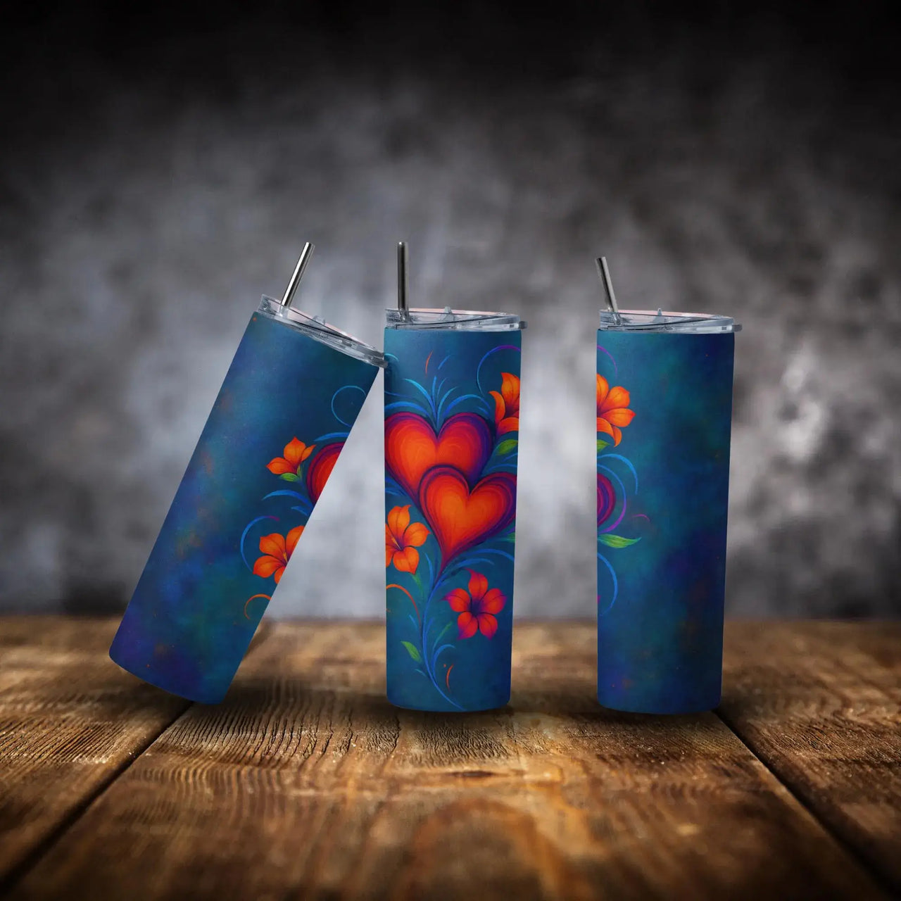 Three blue tumblers with colorful heart and floral designs on a wooden surface.