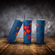 Three blue tumblers with colorful heart and floral designs on a wooden surface.