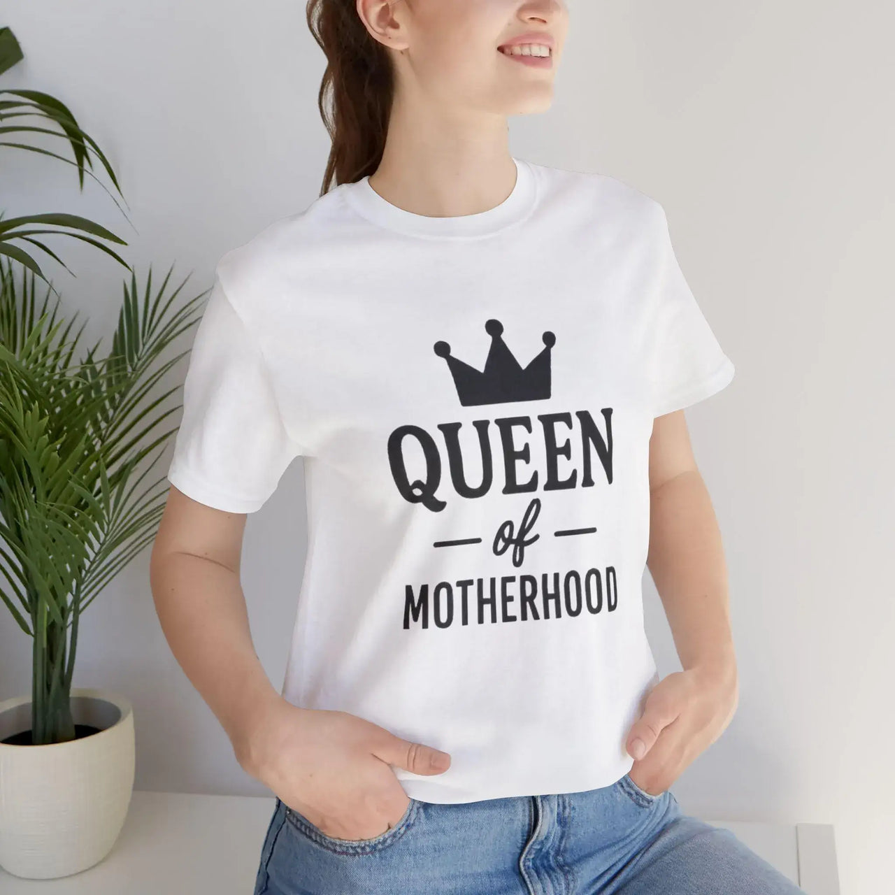 Person wearing a white t-shirt with 'Queen of Motherhood' text and a crown graphic.