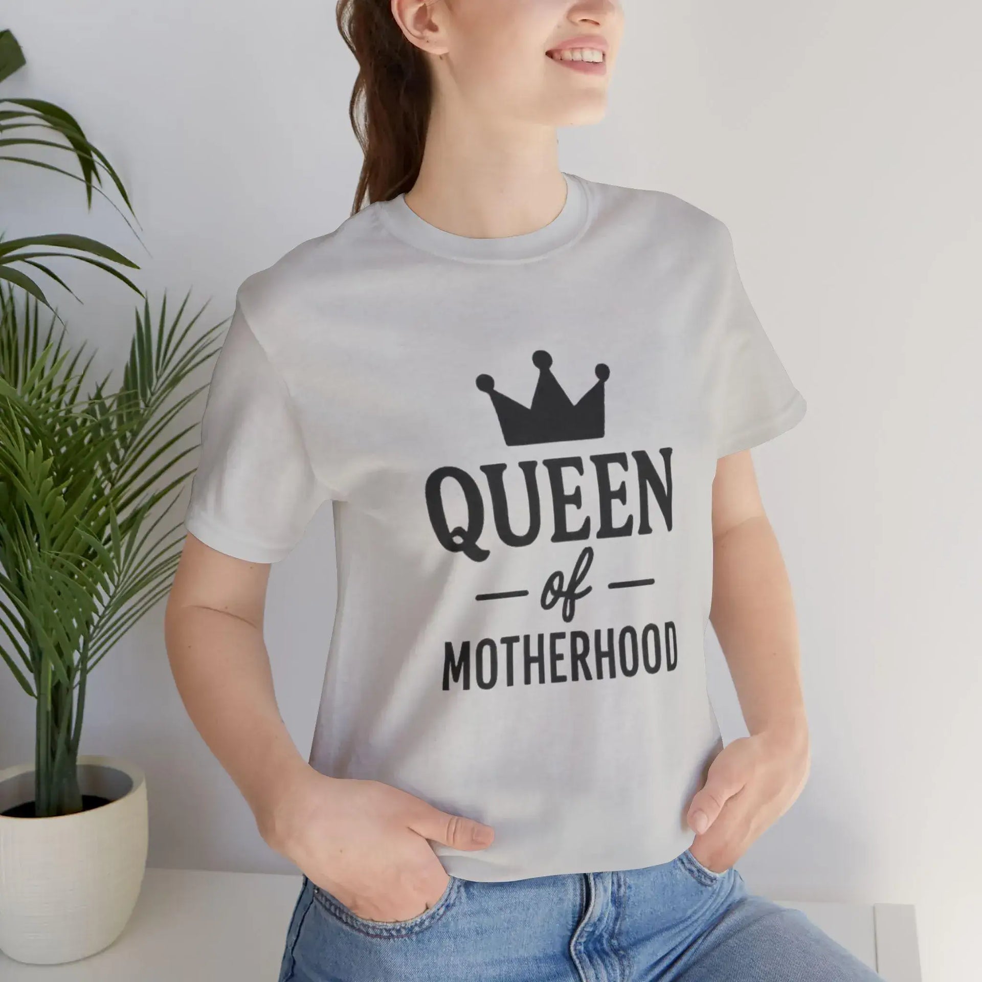 Person wearing a white t-shirt with 'Queen of Motherhood' text and a crown graphic.
