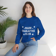 Person wearing a blue sweatshirt with 'MAIN CHARACTER CLUB' text, sitting indoors.