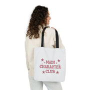 Person holding a tote bag with 'Main Character Club' text and star designs.