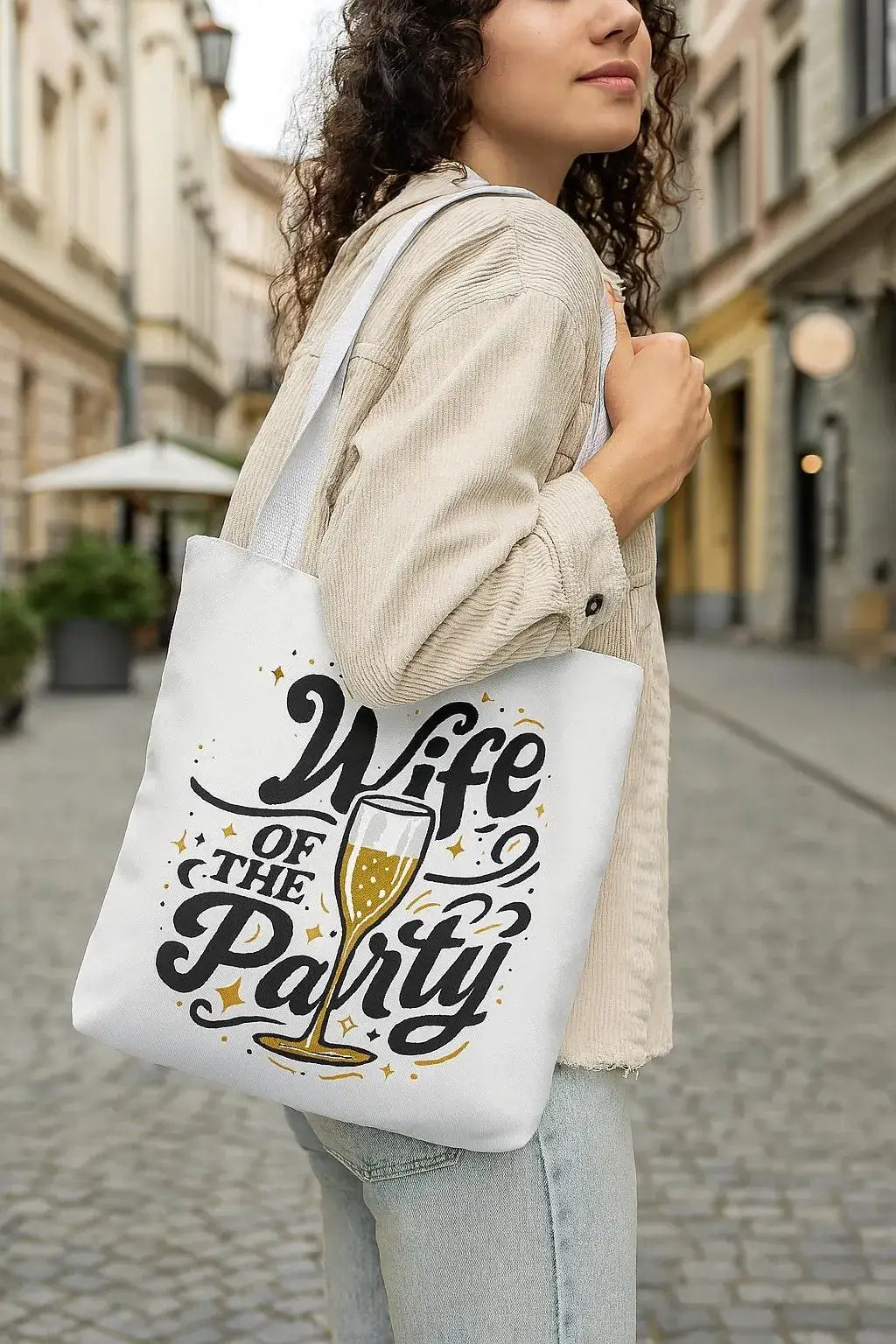 Woman holding a tote bag with 'Wife of the Party' text and champagne glass design on a city street.