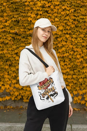 Person holding a white tote bag with a design against a yellow leafy background