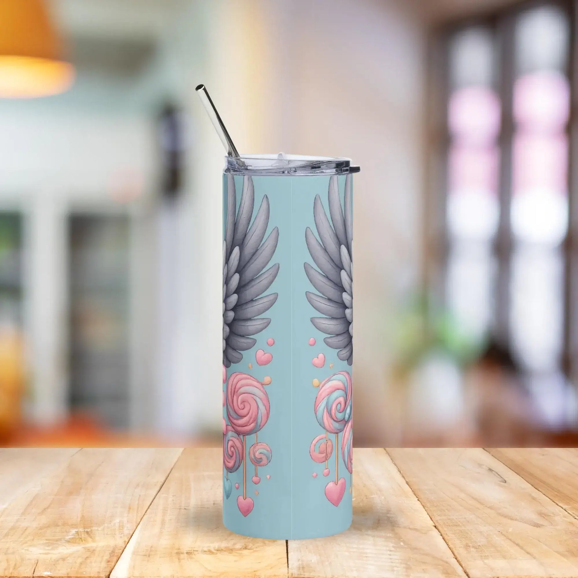 Tumbler with angel wings and heart designs on a light blue background, placed on a wooden surface.