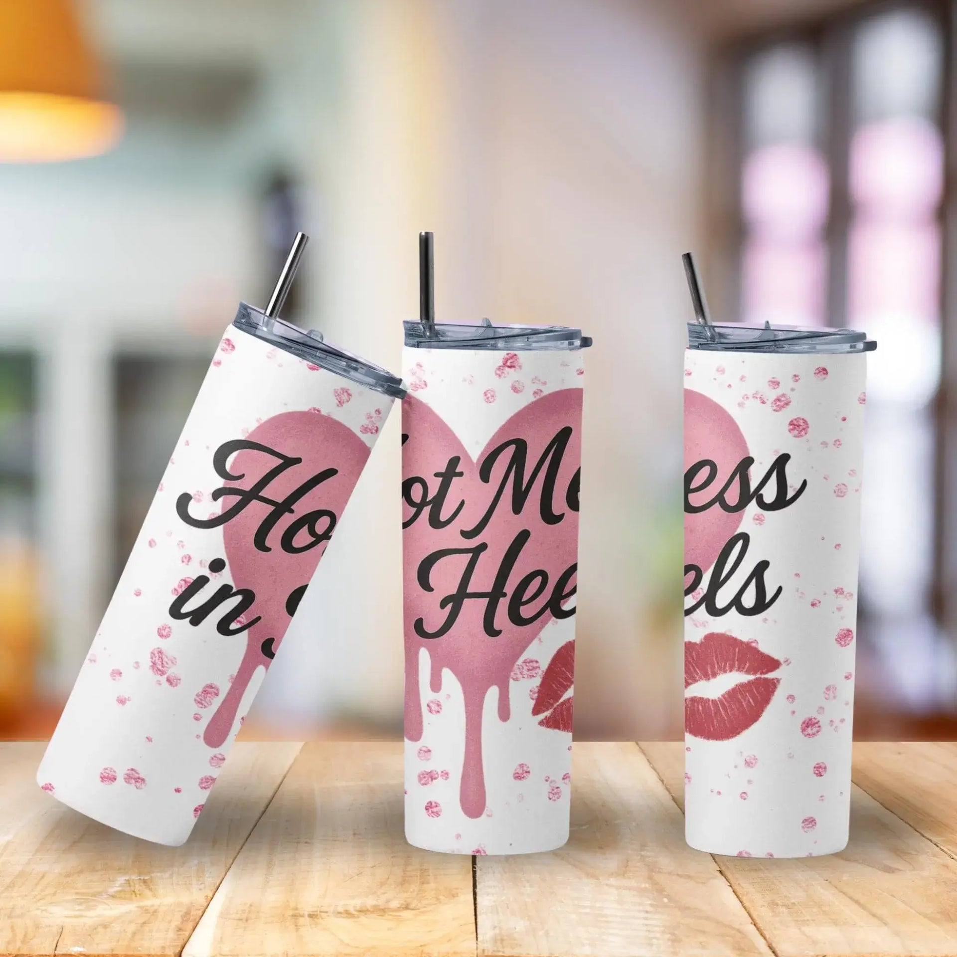 Three tumblers with pink heart and lip designs on a wooden surface.