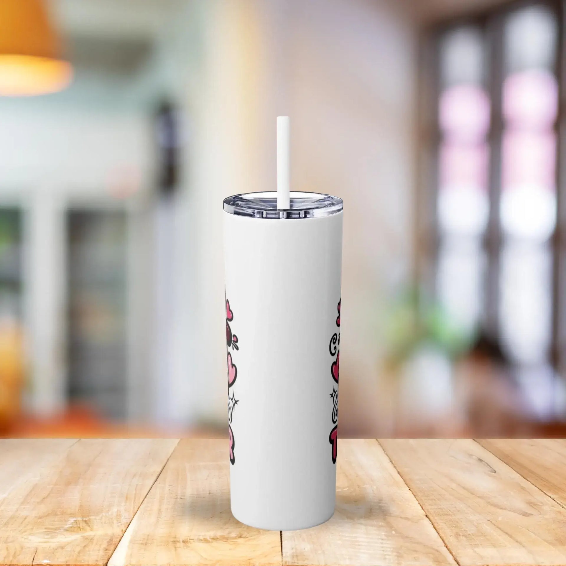 White tumbler with a straw on a wooden table in a blurred indoor setting