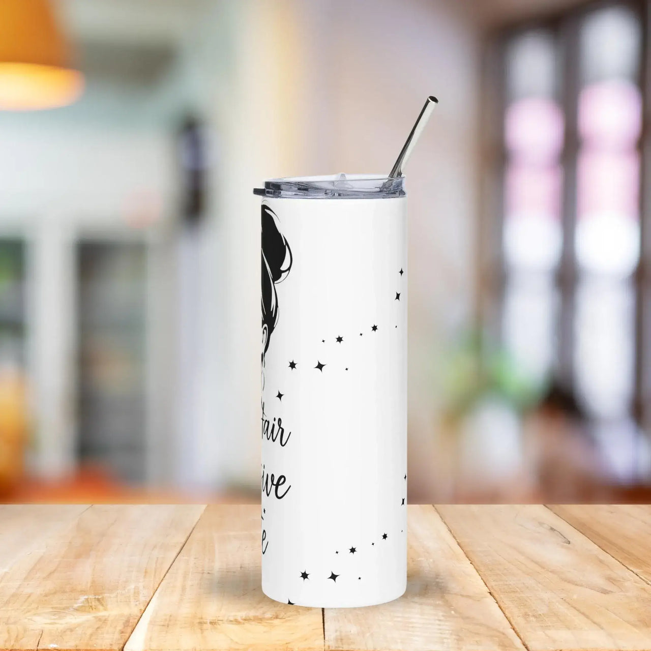 White tumbler with black text and design on a wooden table with a blurred background