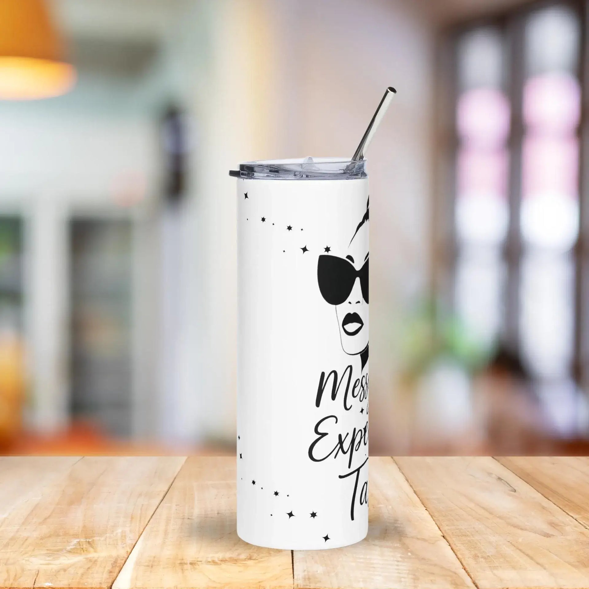 White tumbler with black text and design on a wooden table with a blurred background