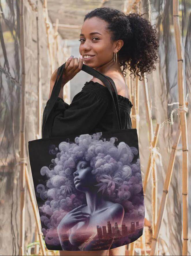 Woman holding a tote bag with a artistic design of a woman with an afro and cityscape.