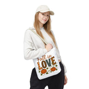 Person holding a tote bag with 'Fall in Love' text and pumpkin design on a white background