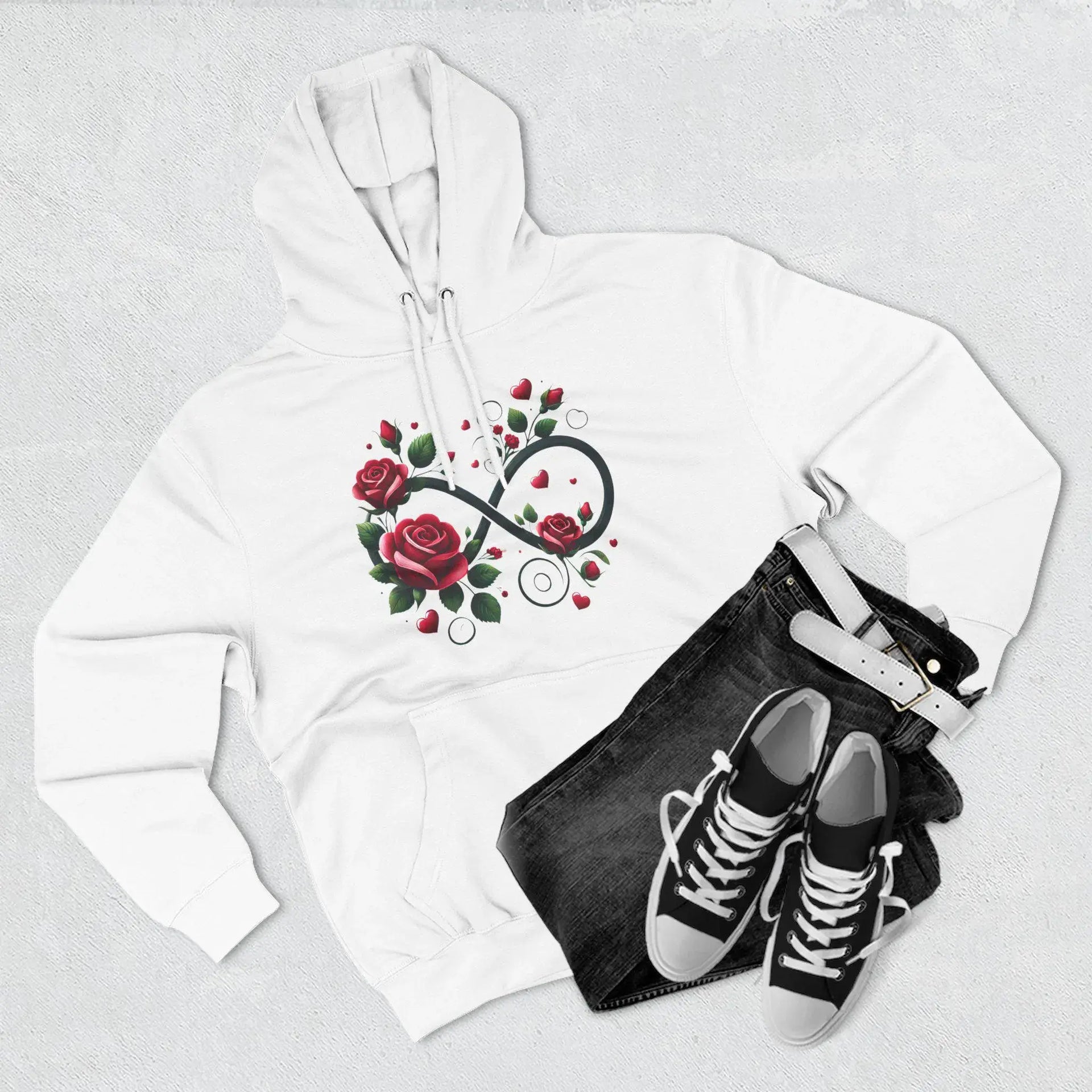 White hoodie with floral infinity symbol design, black jeans, and black sneakers on a light gray background