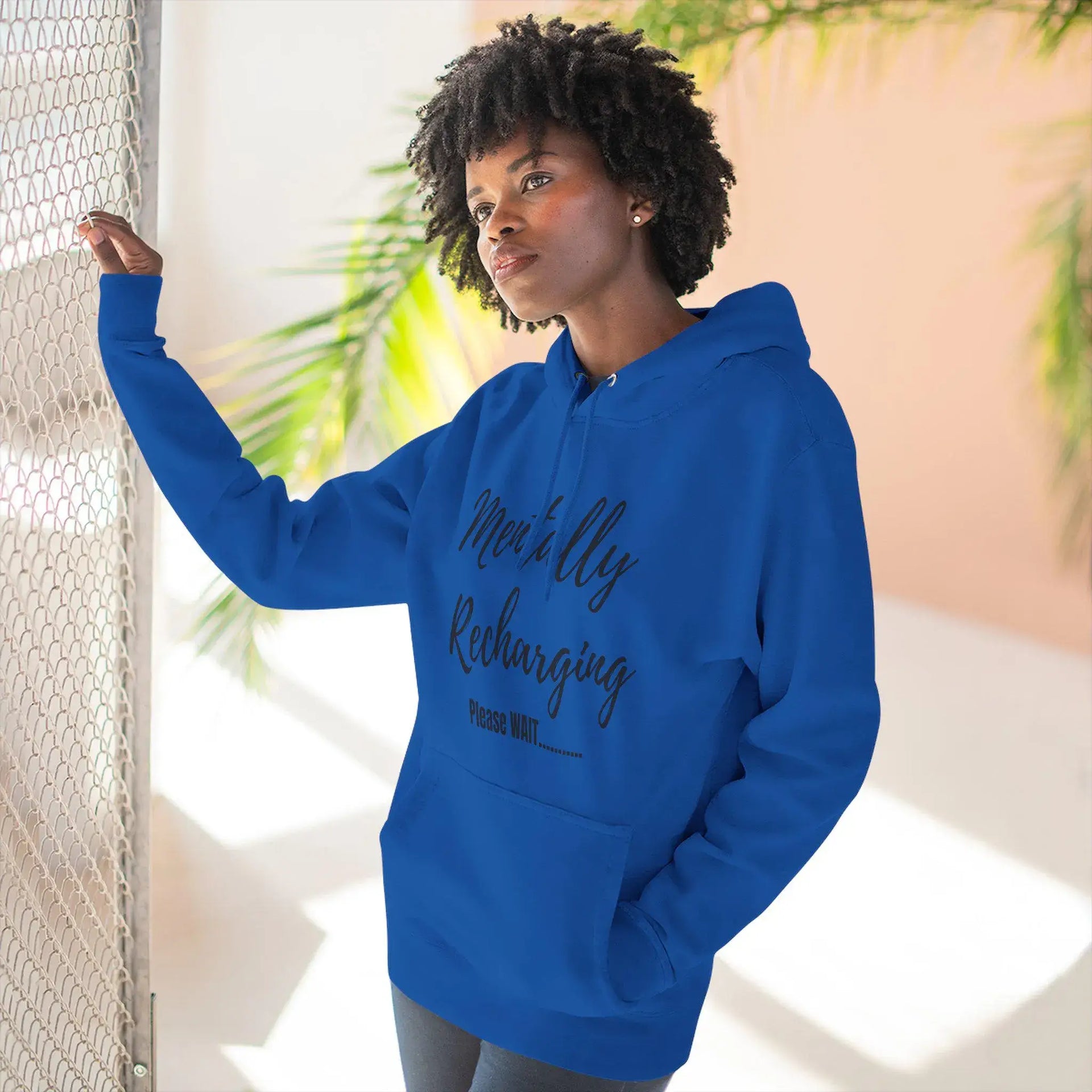Person wearing a blue hoodie with text, standing indoors with plants in the background