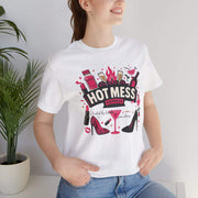 Person wearing a white t-shirt with 'Hot Mess' graphic design, standing indoors next to a plant.