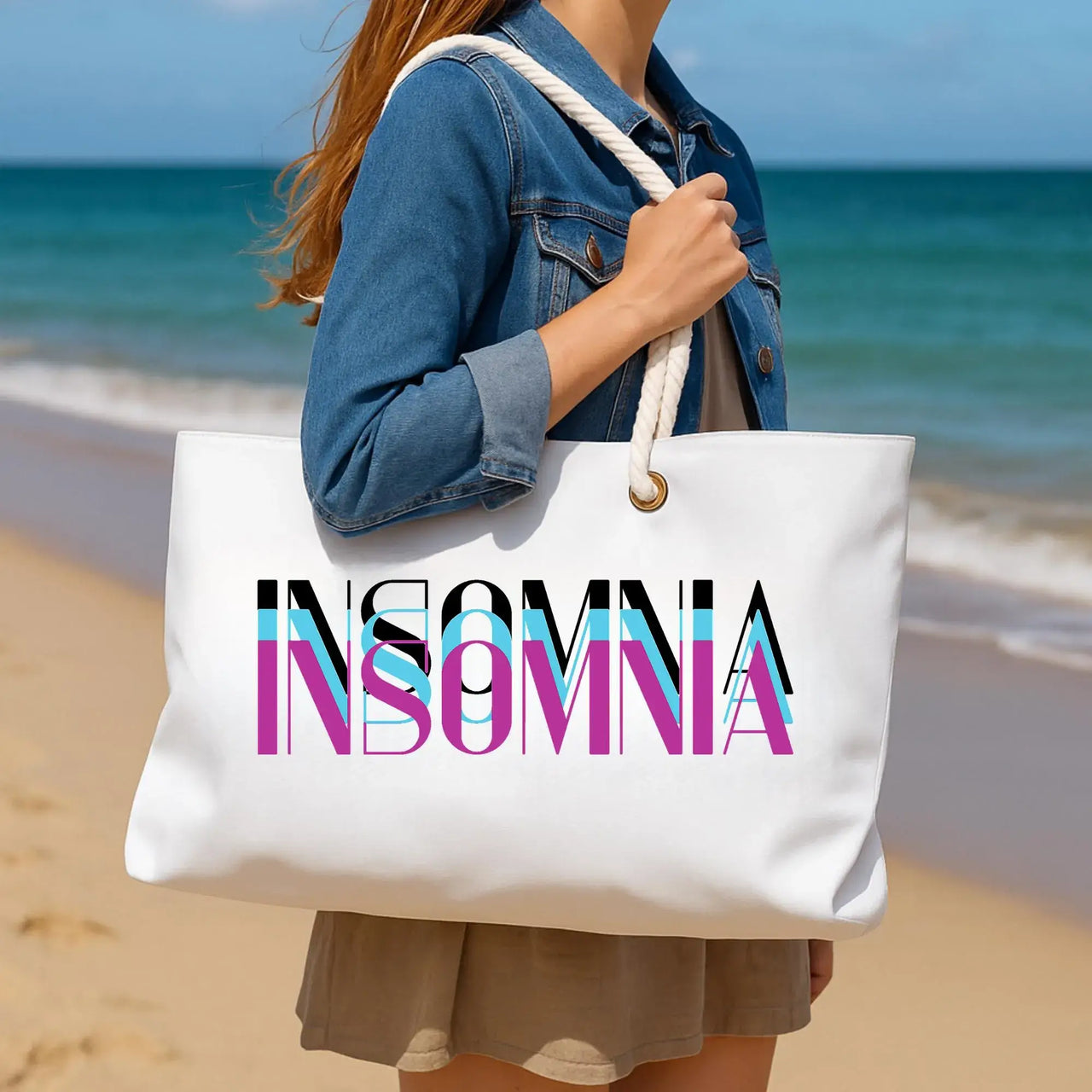Person holding a white tote bag with 'INSOMNIA' printed on it at the beach.