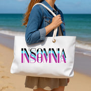 Person holding a white tote bag with 'INSOMNIA' printed on it at the beach.