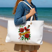 Person holding a white tote bag with red roses and text design on a beach.