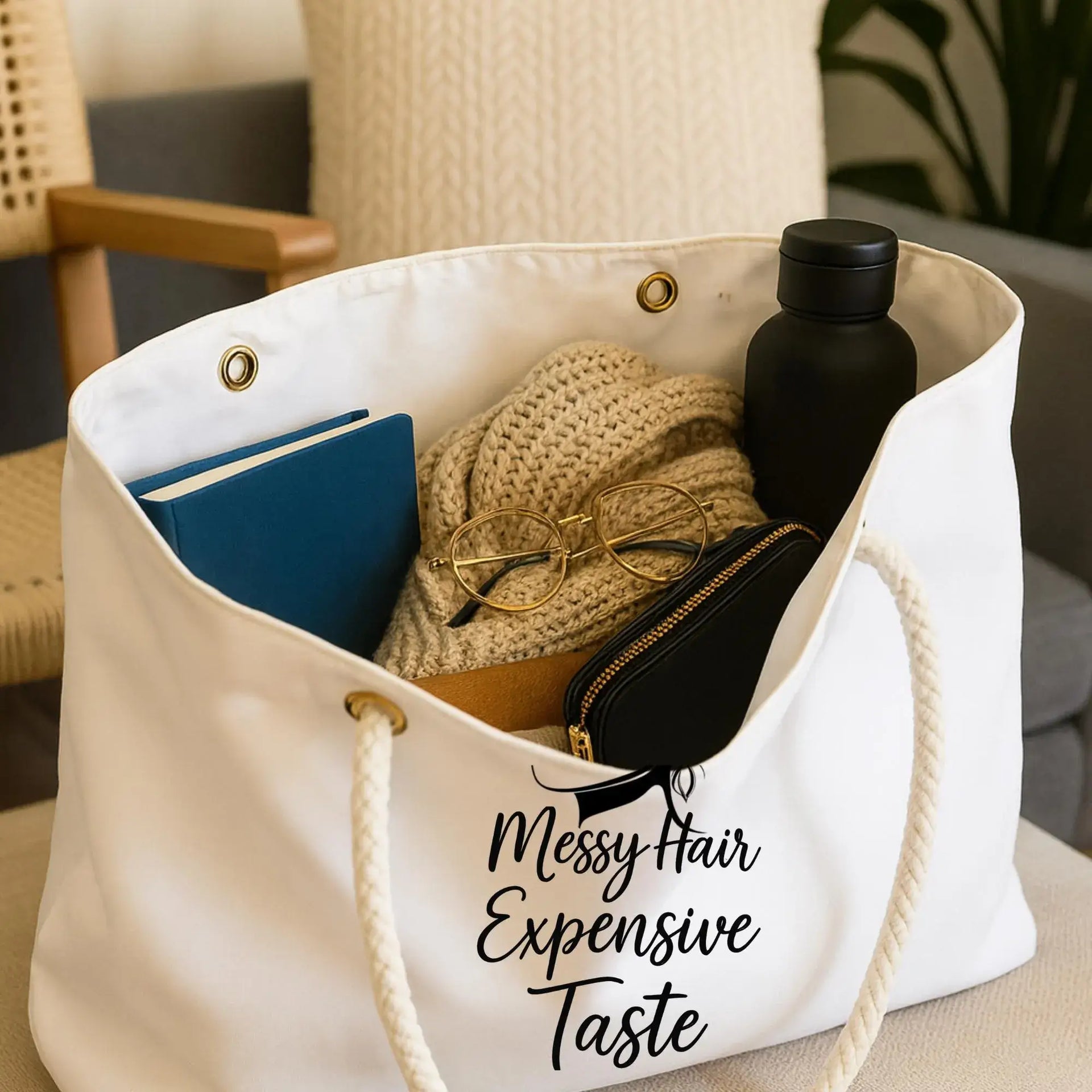 Beige tote bag with various items and humorous text on a blurred indoor background