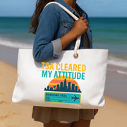 Person holding a tote bag with 'TSA Cleared My Attitude' design on a beach.